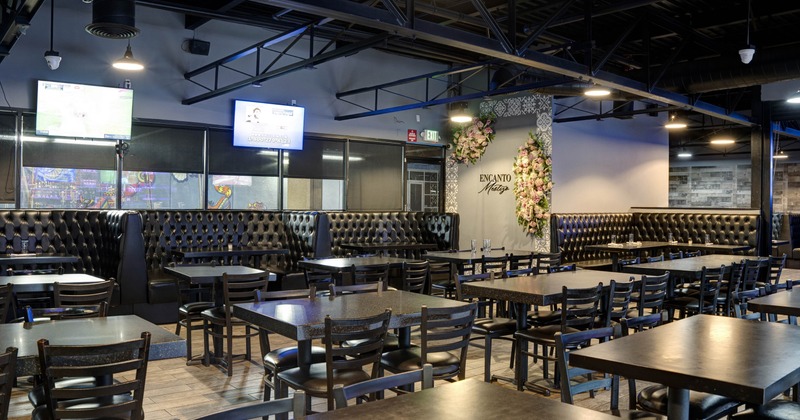Interior with black tables, chairs and booths, red tiled wall and flat screen TVs