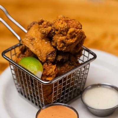 Crispy fried chicken wings in a wire basket, served with two dipping sauces.