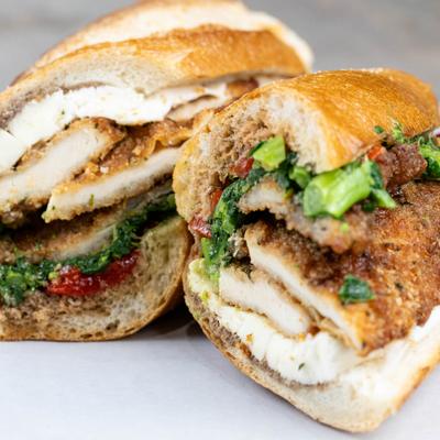 Halved chicken cutlet sandwich with roasted red peppers and broccoli rabe.
