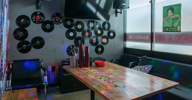 Karaoke room with vinyl records on the wall, a wooden table and cushioned seats