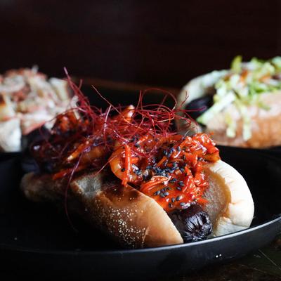 Gourmet hot dog topped with spicy kimchi, sesame seeds, and chili threads.