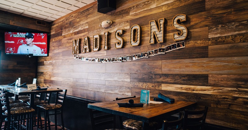 tables by a wooden wall with TV and Madisons wall sign