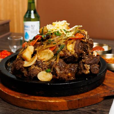 Korean braised beef short ribs served in a cast-iron skillet with vegetables and garnishes.