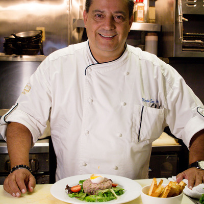 Smiling chef in a white uniform presents a plated meal.