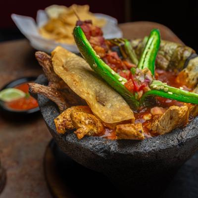 Molcajete with grilled meats and green peppers, served with tortilla chips.