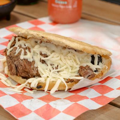 Arepa with shredded beef and melted cheese on a red and white checkered paper.