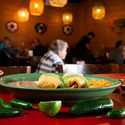 A plate of chimichangas with rice, and beans, set against a lively restaurant backdrop.