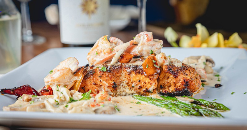 Seared salmon topped with creamy seafood sauce and asparagus served on a white plate