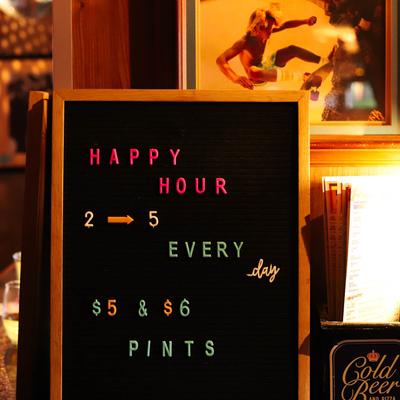 A wooden board displaying happy hour hours and offerings.
