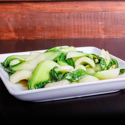Stir-fried bok choy on a table against a wooden wall.