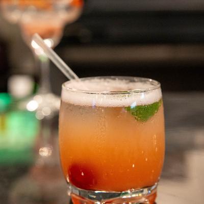 A peach-colored cocktail, garnished with a cherry and mint.