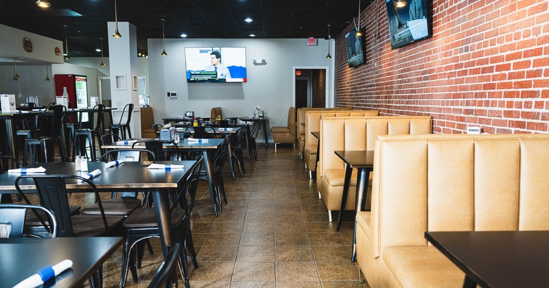 Interior of a modern restaurant with tan booths, black tables and chairs, a red refrigerator