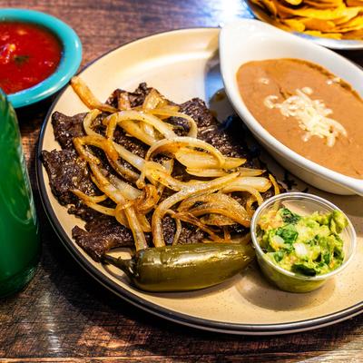 Mexican-style grilled skirt steak topped with onions, served with beans and guacamole.