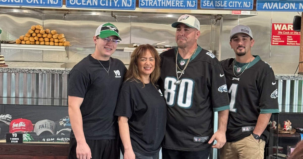 Four people posing in front of a wall adorned with sports memorabilia