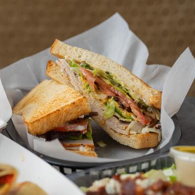 Turkey sandwich basket among assorted food plates, close up.