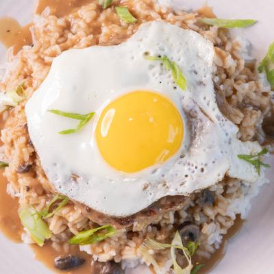 Beef patty, on a bed of rice, with mushroom gravy, sunny side egg, and scallions.