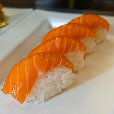 Four pieces of fresh salmon nigiri sushi are arranged on a plate.