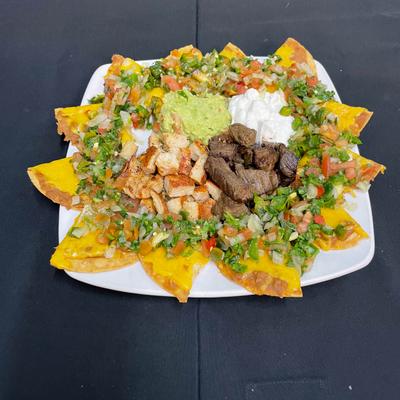Plate of fully loaded nachos with various meats and sauces.