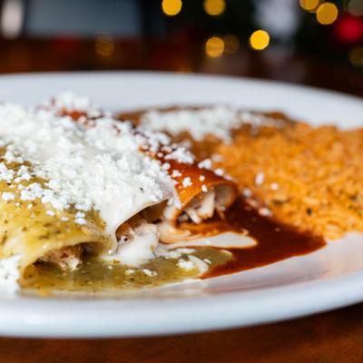Enchiladas, topped with white, green, and red sauces, served with rice and beans.