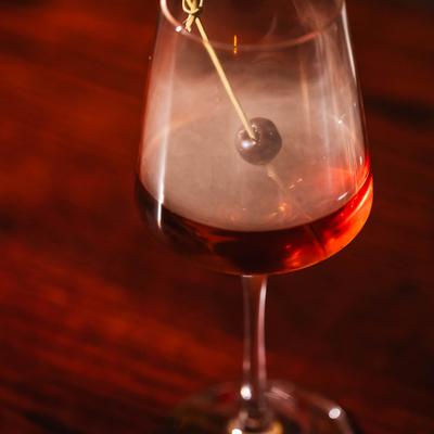 Smoked Manhattan cocktail garnished with a cherry on a pick.