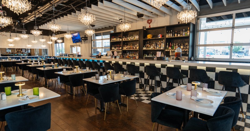 Modern restaurant interior with elegant chandeliers, white topped tables, black chairs