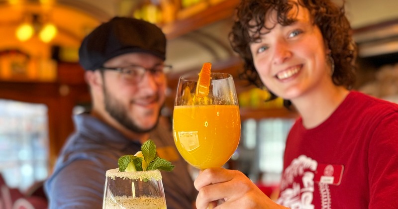 Two staffers smiling, holding colorful cocktails