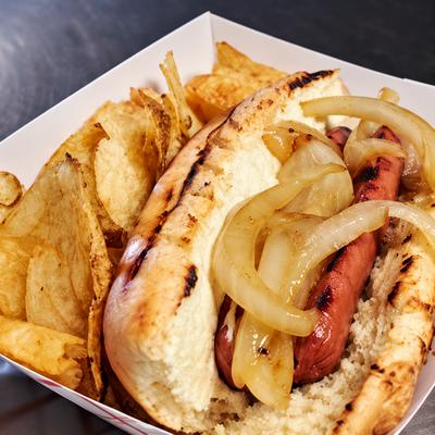 A loaded hot dog with grilled onions served with potato chips..