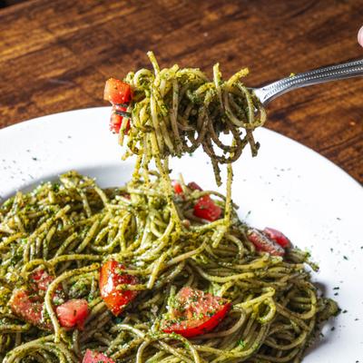 Fork with a bite of spaghetti with pesto and tomatoes.