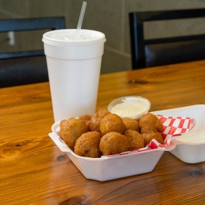 Fried cheese bites and a dipping sauce beside a drink cup.