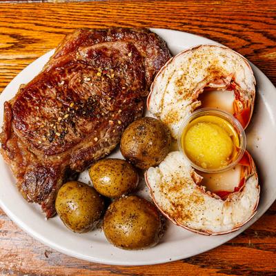 Surf and turf platter featuring ribeye steak, lobster tails, potatoes and melted butter.