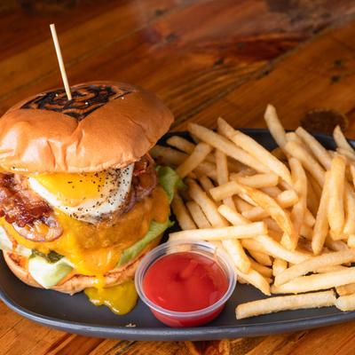 A burger with bacon, avocado, and a fried egg, served with fries and ketchup.