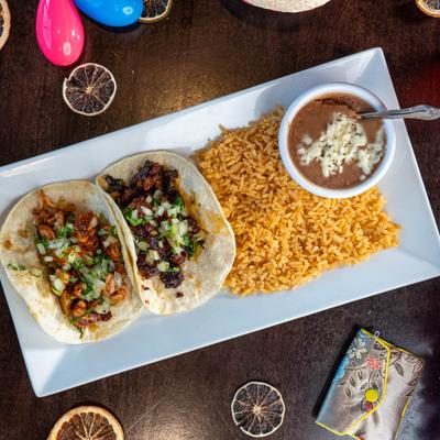 Two tacos on a plate with rice and beans, top view.