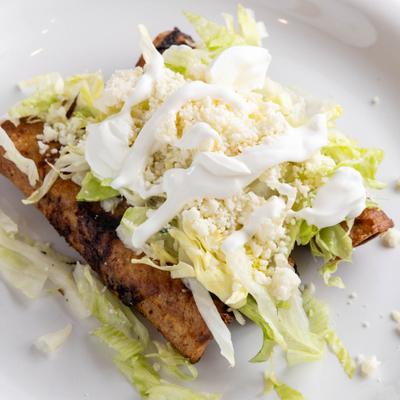 Crispy fried rolled tortillas topped with shredded lettuce, crumbled cheese, and crema.