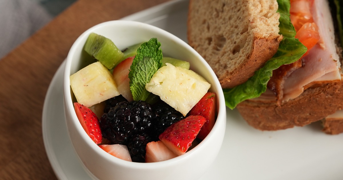 A side of various fruits and the club sandwich