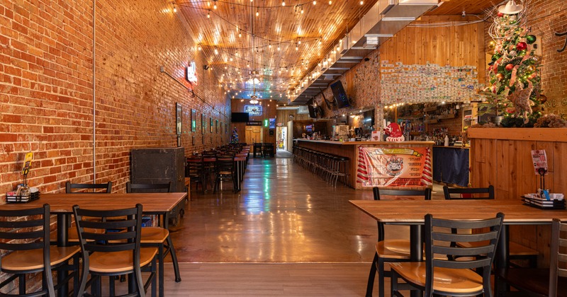 Interior, open space dining area, tables with chairs, long bar with stools, brick walls