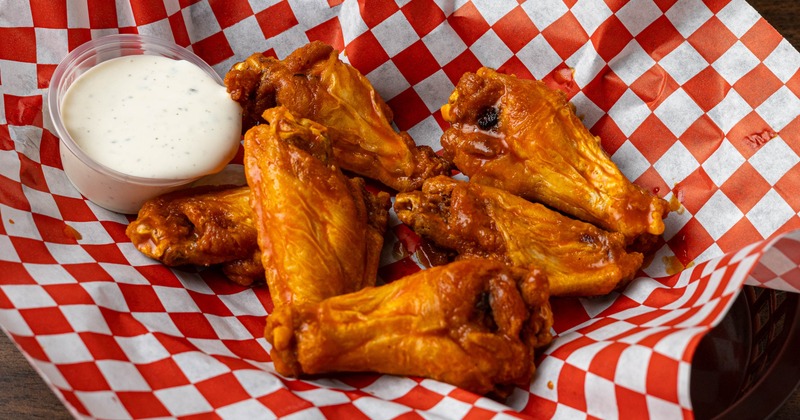 Buffalo Wings and a dipping sauce served on a checkered wax paper