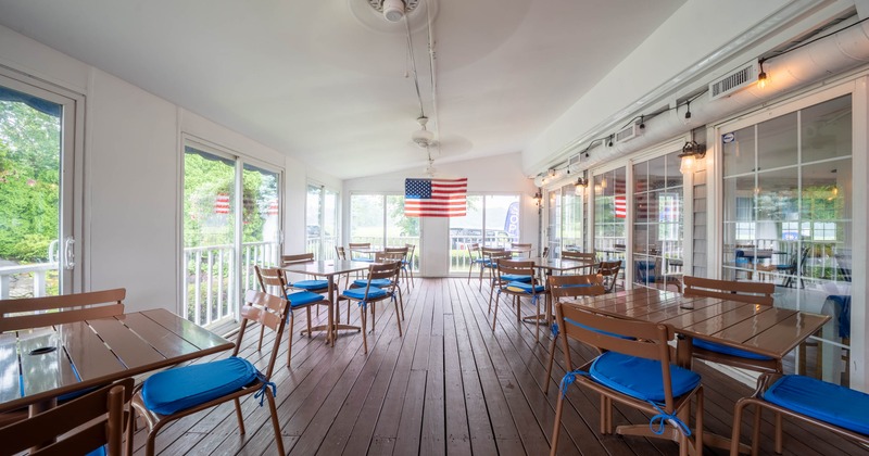 Interior dining space with wooden flooring, tables with blue cushions, large glass doors