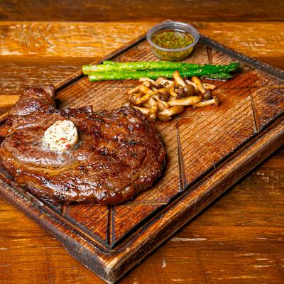 Angus Beef Ribeye served with grilled asparagus and fries on a wooden board.