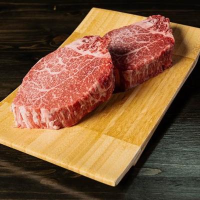 Two  beef steaks  displayed on a wooden cutting board on a wooden table.