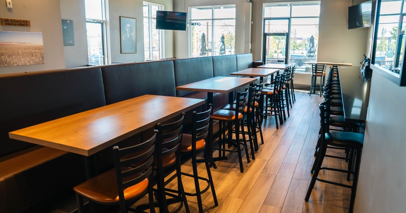 Modern restaurant interior with wooden tables, black chairs, upholstered booths