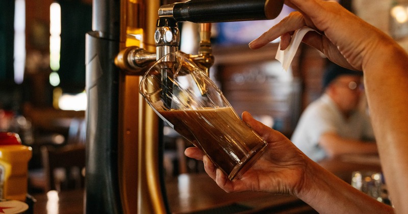 A bartender pouring dark beer from a tap into a glass