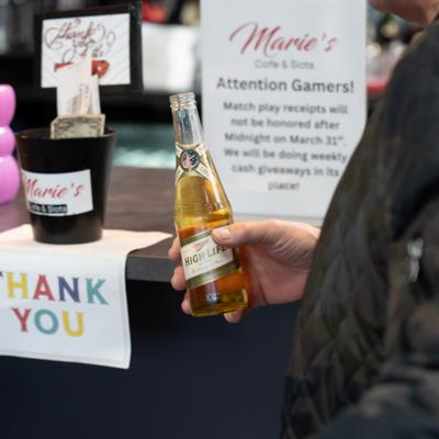Person holding a bottle of beer by the counter with tip jar and Thank You note.