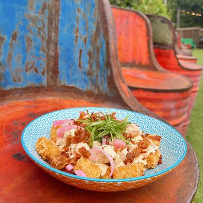 A colorful bowl of tater tots topped with bacon, pickled onions, and mayo.