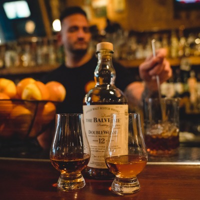 Two Glencairn glasses with straight whiskey and a whiskey bottle behind them.
