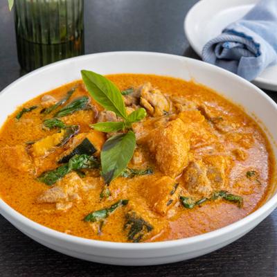 Bowl of Thai red curry with chicken, garnished with fresh basil leaves.