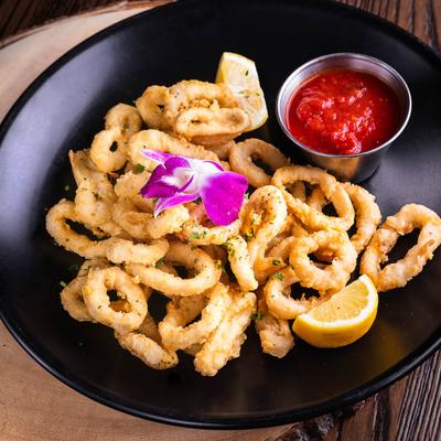 Fried calamari rings on a black plate, accompanied with marinara sauce.
