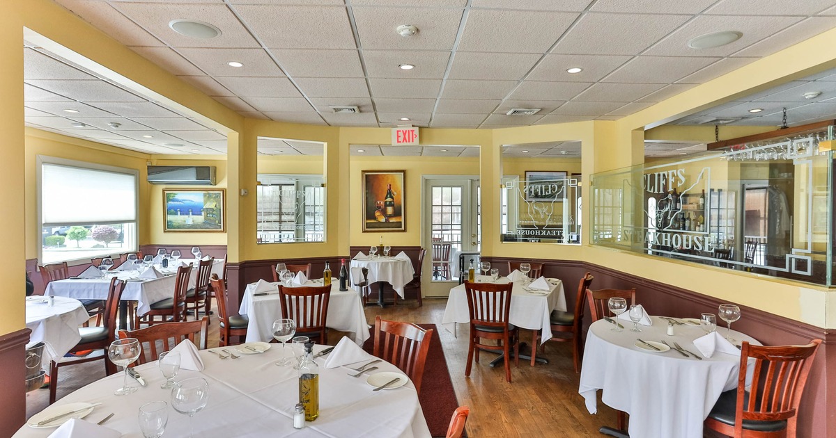 Interior of an elegantly set restaurant dining area with white tablecloths, wooden chairs