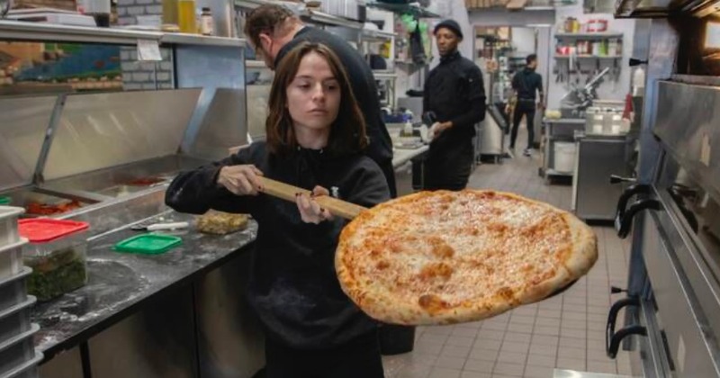 Kitchen interior with employees, one of them holding a pizza peel with a pizza