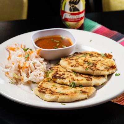 Pupusas served with curtido and a small bowl of tomato salsa.