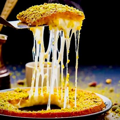 Golden kunafa slice with a crispy pistachio top is lifted, revealing gooey, melted cheese strands.